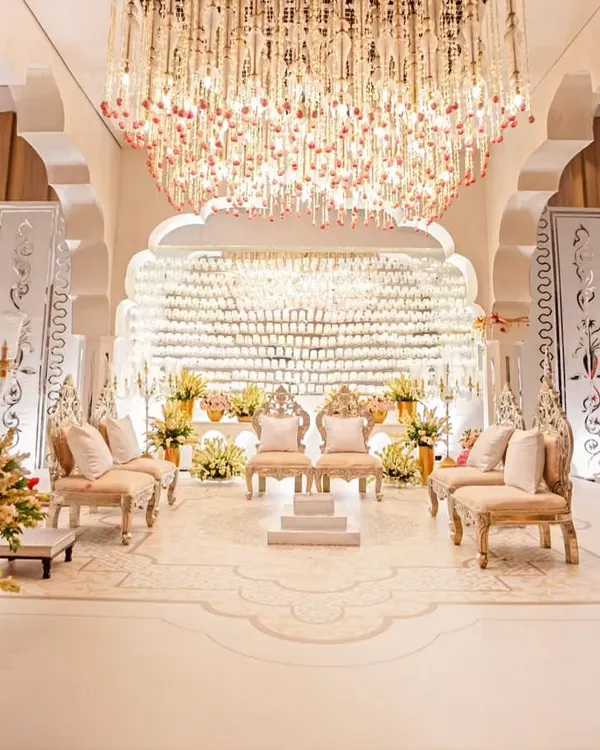 A breathtaking reception stage featuring a backdrop made of 500 crystal glasses. The stage is anchored by ornate seating and a massive floral and crystal chandelier, creating an atmosphere of pure opulence and light.