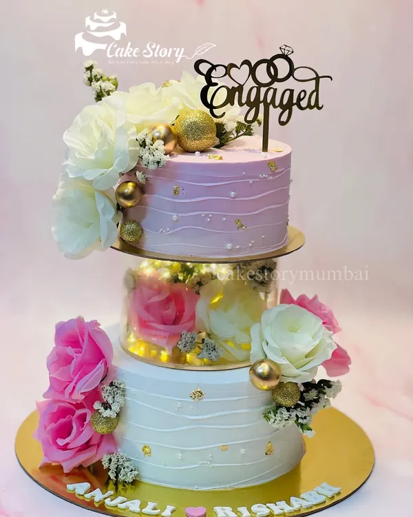An absolutely stunning floral engagement cake. This three-tier creation features a separator filled with lights and flowers, with pink and white ombre frosting and delicate gold leaf accents.