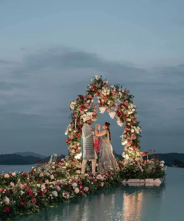 A panoramic view of the Varmala ceremony we designed on an infinity pool. The floral arch and aisle appear to float on water, creating a breathtaking backdrop against the twilight sky and the mountains of Wayanad for a truly unforgettable destination wedding.