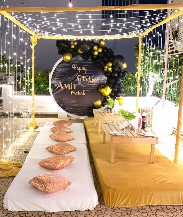 A beautiful rooftop cabana setup for a birthday. This intimate arrangement includes a canopy with fairy lights, low seating with plush cushions, and a personalized backdrop.