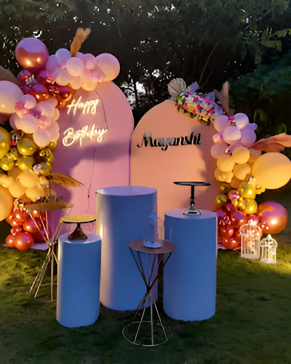 An elegant birthday party setup on a lawn for an evening celebration. This design uses two arched backdrops, a neon sign, and a sophisticated balloon arrangement in warm tones, all beautifully lit.