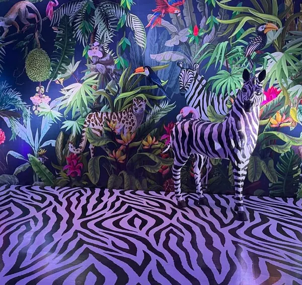 I designed this fully immersive jungle scene with a custom illustrated wall, zebra-print flooring, and a life-sized zebra prop. The moody lighting makes the space feel mysterious and wild.