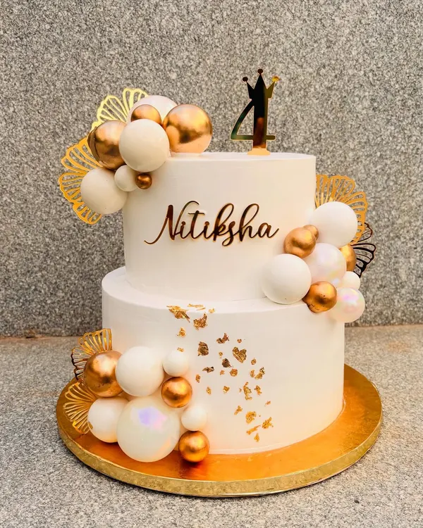 This 5-kilo two-tier cake in white and gold was a showstopper. It's decorated with clusters of white and gold spheres, gold leaf, and a custom name and age topper.