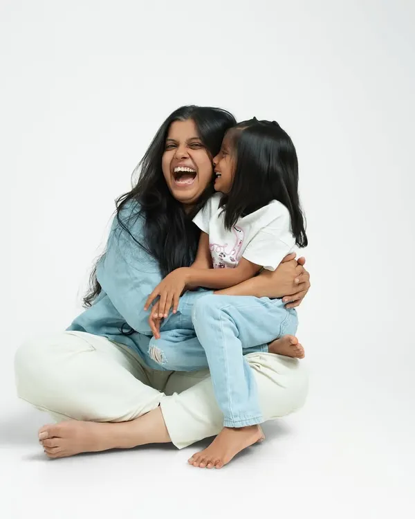 A mother and daughter sharing a moment of pure, uninhibited laughter. The simple white background of the studio puts their joyful connection at the center of the portrait.