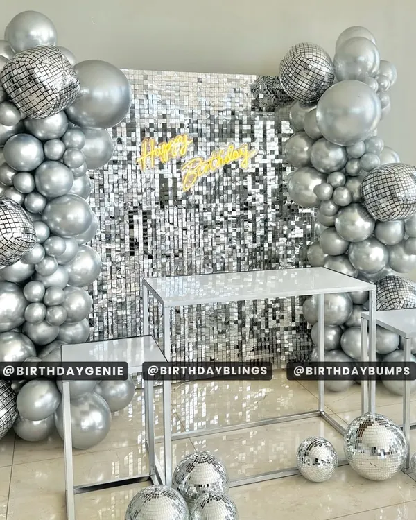 A dazzling disco-themed setup featuring a silver shimmer wall and a matching all-silver balloon arch. The disco ball accents and neon "Happy Birthday" sign complete this groovy party look.
