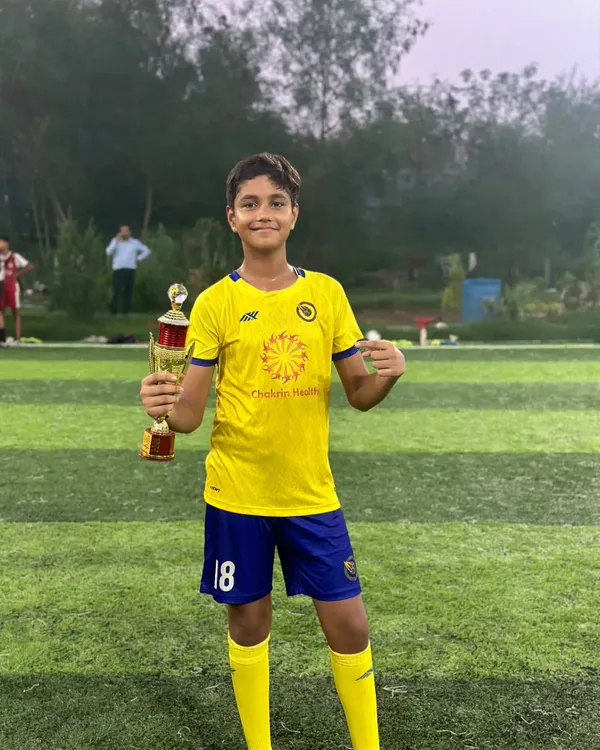 The smile of a champion. A player proudly holds his first trophy, a reward for his hard work and performance.