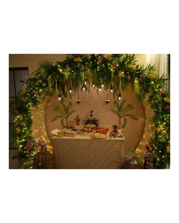 We designed this breathtaking Ganpati mandap, creating a divine focal point for the celebration. The setup features a lush arch of fresh palm leaves and florals, warmly lit by fairy lights and hanging Edison bulbs, all framing a custom-painted backdrop for a truly serene atmosphere.