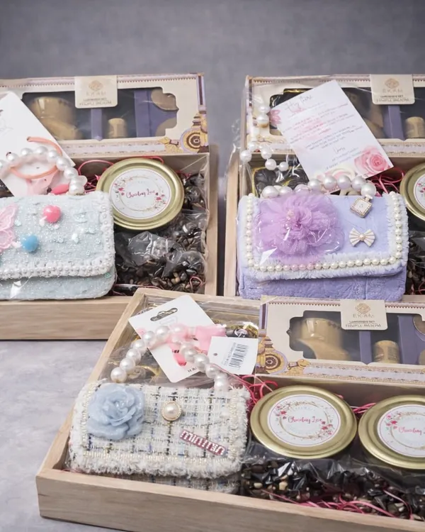 A beautiful collection of birthday hampers for a baby girl. Each wooden tray is filled with an aroma diffuser, chocolates, cookies, and a cute mini handbag, available in different pastel colors.