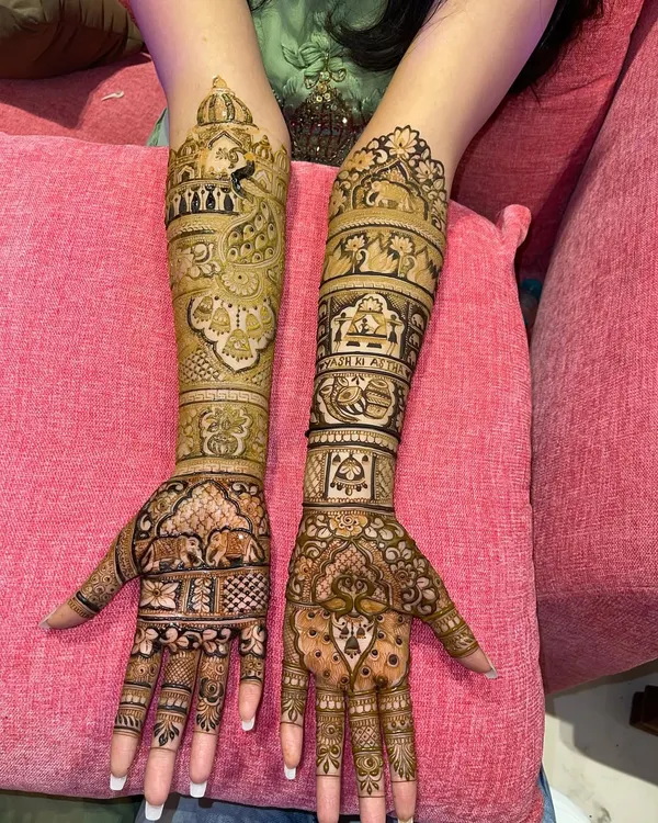 A complete bridal look with matching designs on both arms. This Rajasthani style mehndi is filled with figures, elephants, and architectural details, ensuring a grand and traditional look for the bride.