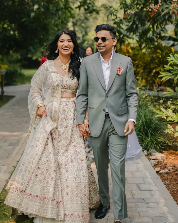 A bespoke sage green suit, crafted from a Super 130s merino wool blend, perfectly complements the bride's floral lehenga for a beautiful day wedding. This is what it looks like when your outfit is in perfect sync with the moment, and with her.