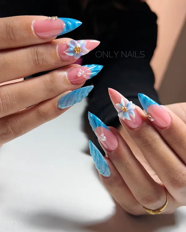 An example of extreme, sculpted nail art. This set features long stiletto extensions with a blue French tip, marbled accent nails, and large, 3D sculpted flowers.