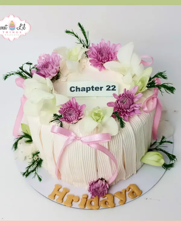 This elegant "Chapter 22" cake is a beautiful way to mark a new year. The design features a delicate pleated frosting effect, soft pink ribbons, and a crown of fresh, beautiful flowers like orchids and chrysanthemums.