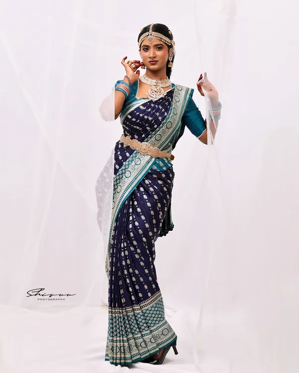 A full-length professional shot showcasing a complete look. The navy blue and teal saree is draped to perfection, complemented by traditional jewelry and a confident pose.