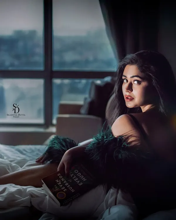 A moody and intimate portrait of actress Ritabhari Chakraborty. The soft light from the window and the cozy bedroom setting create a contemplative and personal atmosphere.