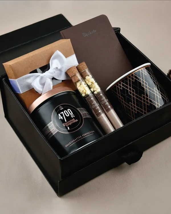 Our "Cozy Vibes" gift hamper, featuring gourmet popcorn, hot chocolate test tubes, a notebook, and a stylish mug.