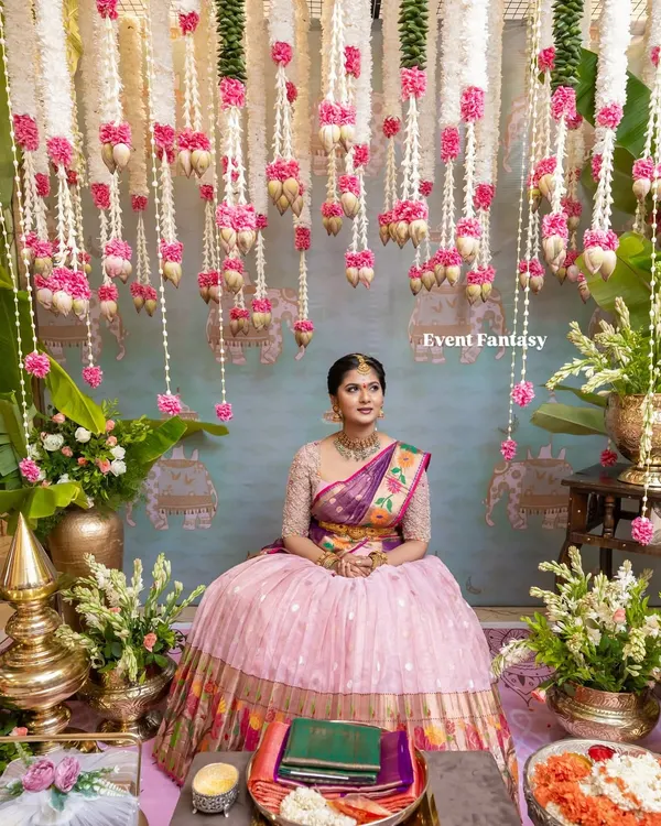 The bride, looking serene and beautiful, seated for her pre-wedding rituals. I created a stunning backdrop with hanging garlands of jasmine, lotus buds, and pink carnations, set against a custom-painted traditional mural.