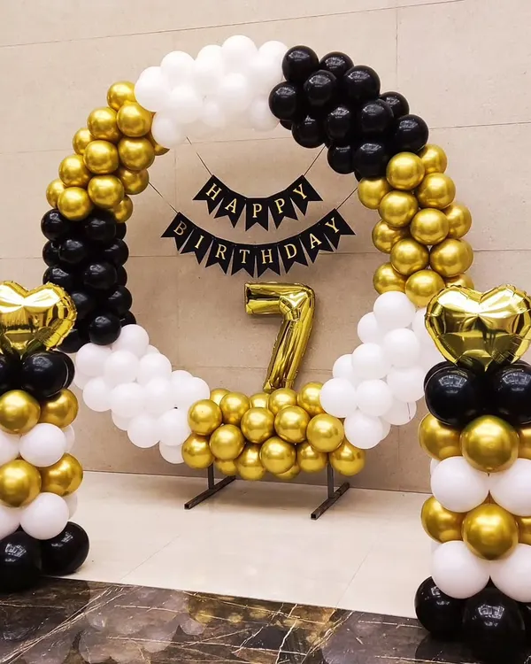 A chic and modern birthday setup using a circular balloon arch in black, white, and gold. This clean design is perfect for any age and includes a 'Happy Birthday' banner and a large foil number.