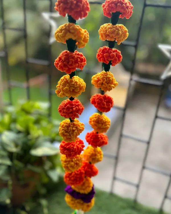 A close-up of my crochet marigold garland hanging by a window. The alternating yellow and orange flowers look just as fresh and vibrant as real genda phool, bringing cheer to any space.