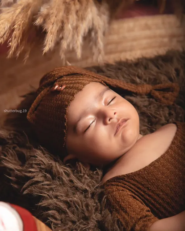 A close-up of a sleeping three-month-old boy, looking so peaceful in his cozy brown outfit and hat.
