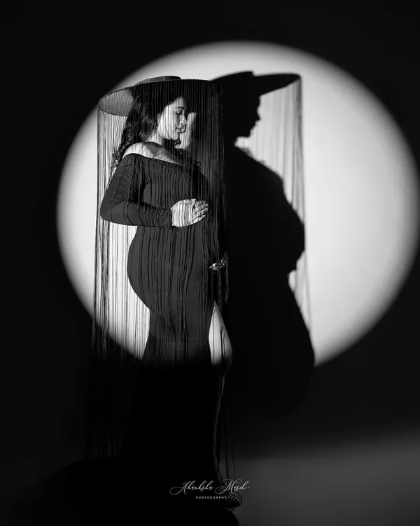 A dramatic black and white portrait using shadow and light. The spotlight creates a powerful silhouette, while the fringed hat adds a touch of vintage mystery and style.