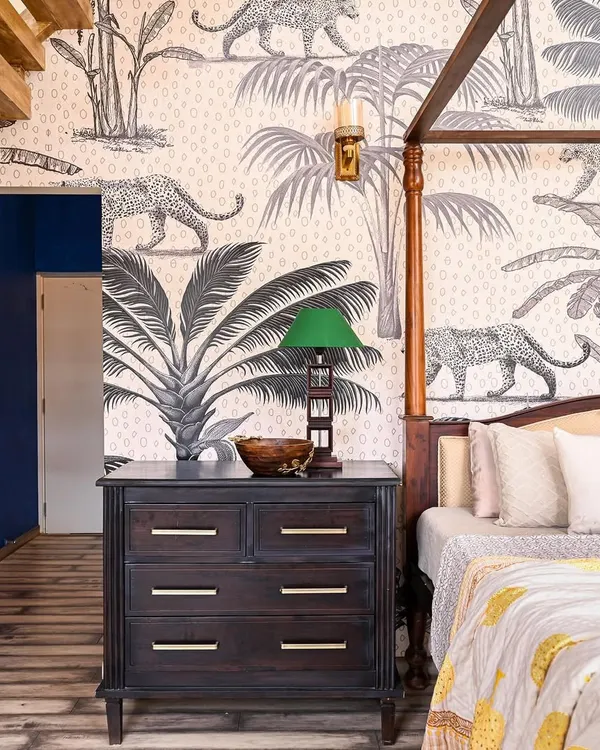 This master bedroom is a room of surprising contrasts. A cantilevered staircase and a bold cobalt blue wall lead into the main space, where a towering 16-foot ceiling is grounded by a four-poster bed. The jungle-themed wallpaper adds a touch of wildness, creating a dramatic yet deeply personal retreat.