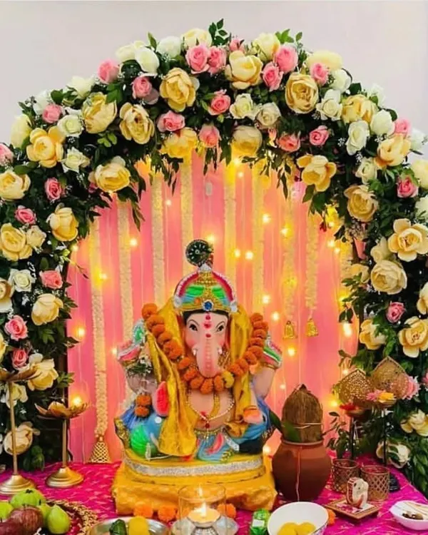 I design classic and elegant Ganpati backdrops. This beautiful setup features an arch of yellow and pink roses over the idol, with a backdrop of delicate string lights that create a warm, divine glow.