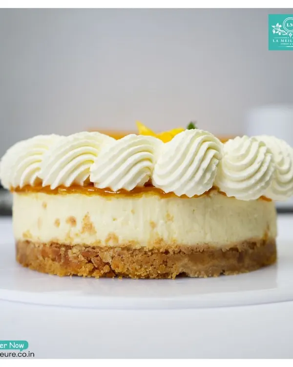 A side view of our creamy Mango Cheesecake. You can see the thick, buttery biscuit base, the rich cream cheese layer, and the fresh mango topping with piped cream.