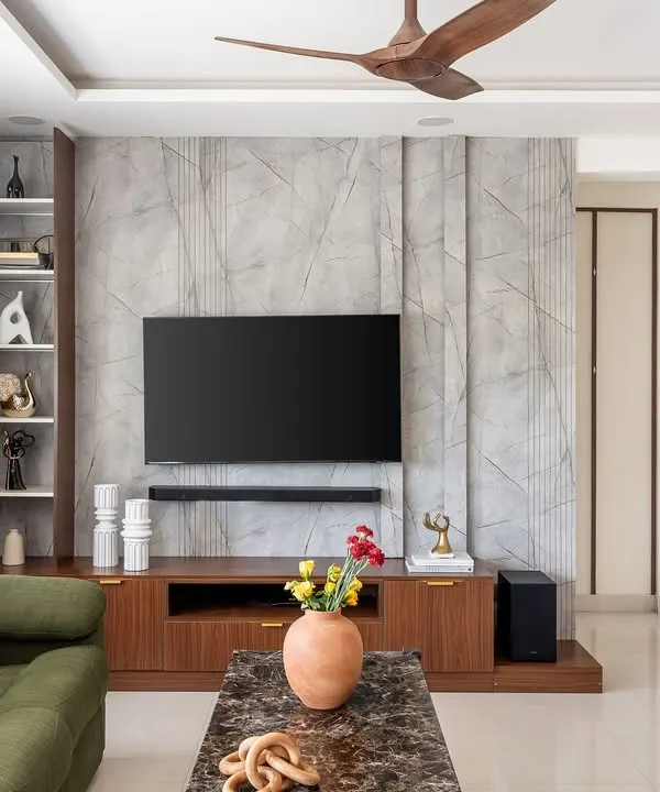 This living room in 'The Flux Abode' project features a textured grey media wall and rich walnut cabinetry. The design combines contemporary sophistication with warm, natural materials for a balanced and inviting feel.