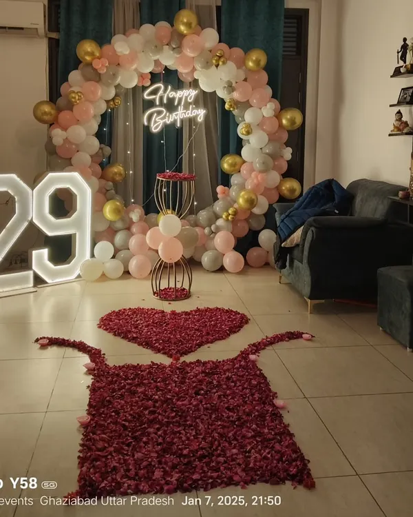 I can transform your living room into a stunning celebration space. This setup for a 29th birthday features a custom circular balloon arch in pastel and gold, a 'Happy Birthday' neon sign, large light-up marquee numbers, and a romantic rose petal pathway.