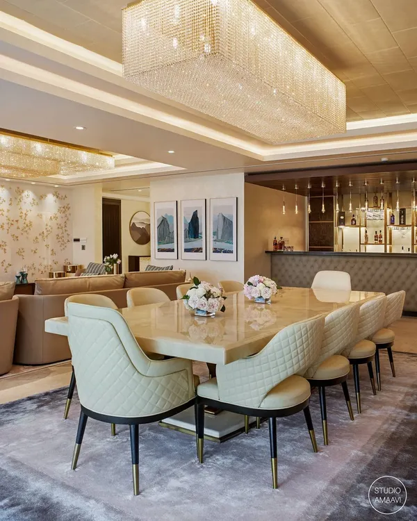 An integrated living, dining, and bar area from our Kingfisher Tower project. The design features a magnificent onyx dining table and quilted leather chairs, unified under a large crystal chandelier that creates a cohesive and luxurious atmosphere for entertaining.