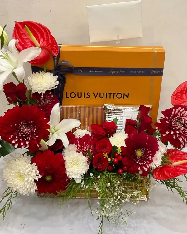 An elegant floral gift hamper featuring a Louis Vuitton box, surrounded by a lush arrangement of red anthuriums, white lilies, and chrysanthemums. A simple yet luxurious statement.