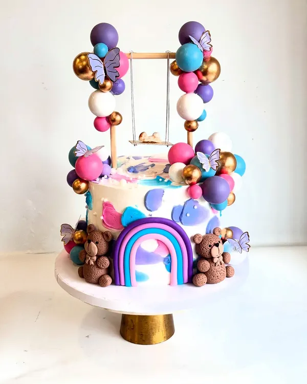 How cute is this swing baby shower cake? This unconventional design features a tiny baby on a swing, surrounded by colorful chocolate balloons, teddy bears, and a rainbow.