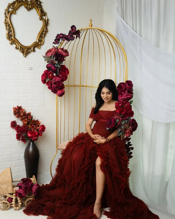 A moment of quiet contemplation in our floral paradise setup. The rich red gown and matching flowers create a stunning, monochromatic look against the golden birdcage chair.