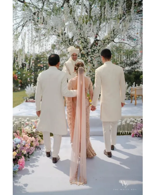 A beautiful moment as the bride walks towards her happily ever after, escorted down a pristine white aisle lined with lush pastel florals. This is the essence of a dreamy garden wedding.