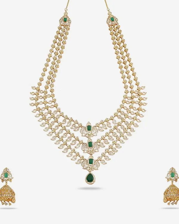 A luxurious three-layer necklace set made with American Diamonds and emerald-colored stones. The set includes matching jhumka earrings, creating a complete and opulent look for a bride or wedding guest.