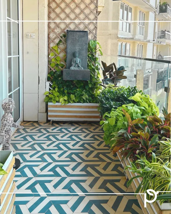 A zen corner created on a balcony, featuring a Buddha water fountain nestled among lush greenery. This design combines geometric floor tiles with custom planters to create a modern yet peaceful retreat.