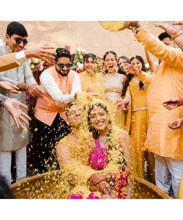 A perfect storm of joy! The couple is showered with flower petals by their loved ones in a moment of pure, chaotic happiness. This is what a fun-filled Haldi ceremony looks like.