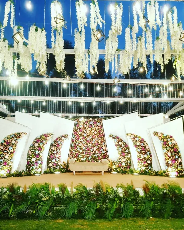 This is a signature outdoor reception stage I designed, featuring a modern, multi-panel floral backdrop. The structure is complemented by dramatic hanging floral installations and professional lighting to create a truly spectacular setting against the night sky.