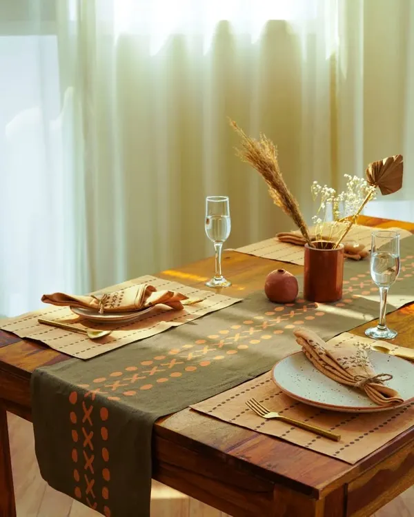 A beautifully set dining table featuring block-printed mats and napkins. The warm, natural light and earthy tones create a homely and inviting atmosphere for this tableware brand.