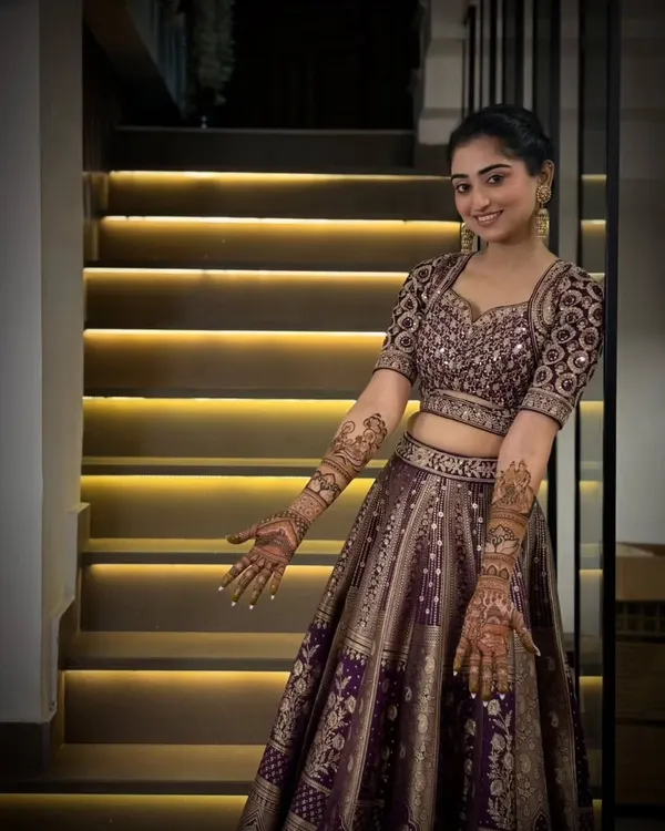 A beautiful, smiling bride in her full wedding attire, proudly showing the intricate mehandi we designed to complete her look.