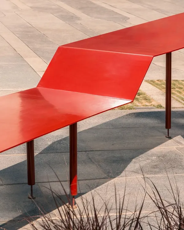 A detail of the Red Ribbon Plaza. The bright red, powder-coated steel is folded to create a continuous surface that functions as both a bench and a table, providing a playful and highly functional piece of urban furniture for a tech campus in Bangalore.