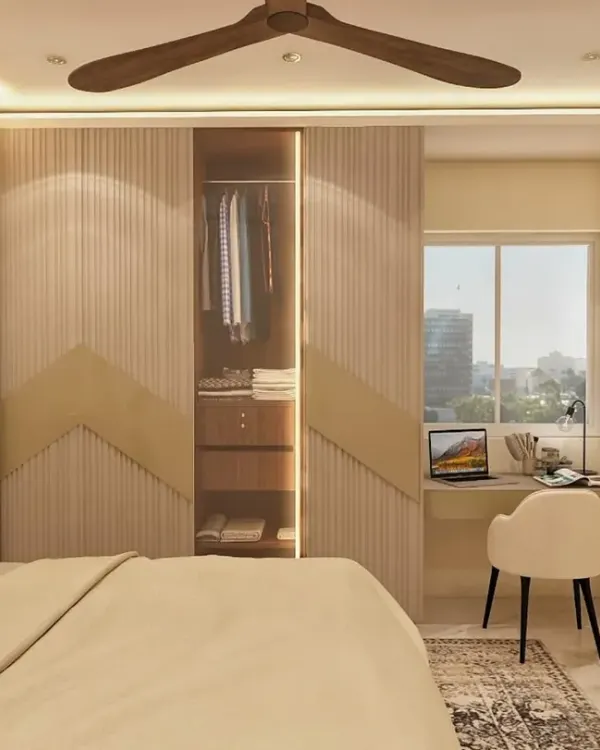 This bedroom design seamlessly integrates a wardrobe with a compact study nook by the window. The fluted and chevron-patterned wardrobe doors add a layer of texture, while the built-in desk provides a functional workspace with ample natural light.