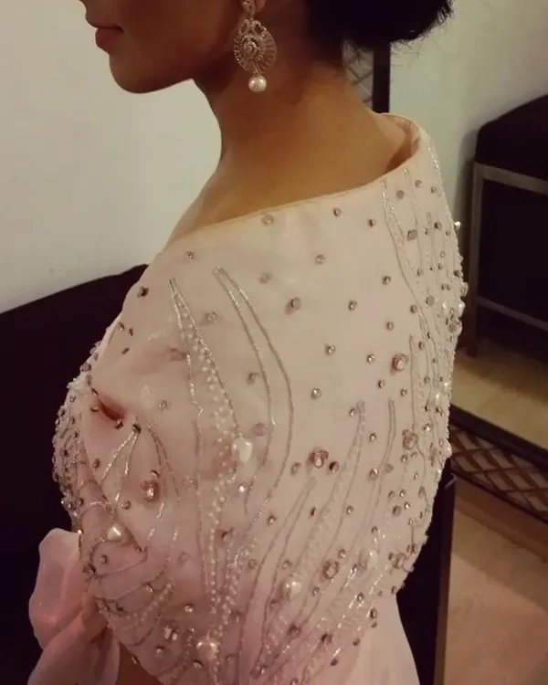 A closer look at the delicate hand embroidery on the pink gown. Each pearl and sequin is carefully placed to create a soft, dreamy effect on the off-shoulder cape.