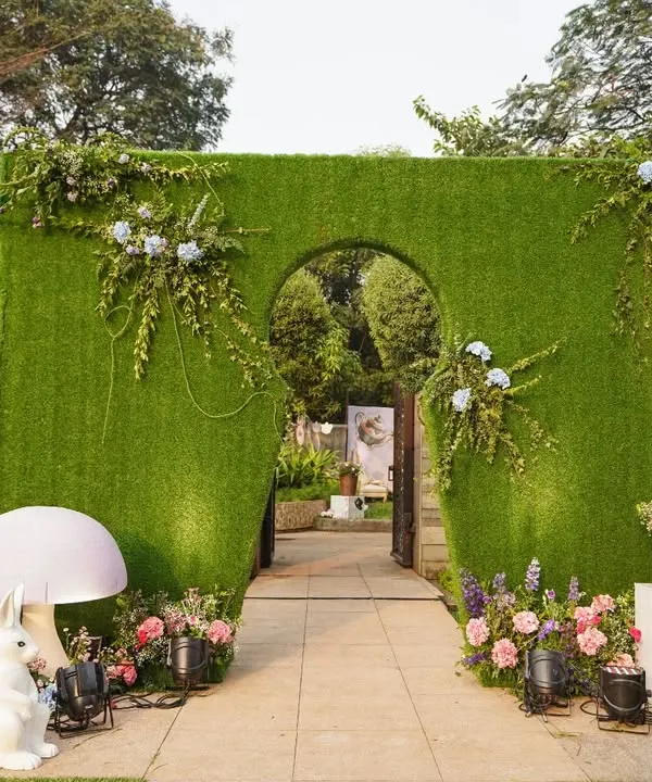 Welcome to Wonderland. The entrance to this themed baby shower features a grass wall with a keyhole arch, flanked by whimsical props like the White Rabbit and giant mushrooms.