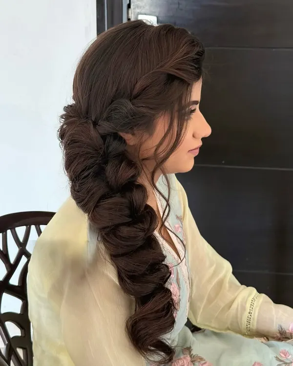 Braided with love. This thick, side-swept braid is full of texture and volume, making it a stunning choice for a Mehendi or Sangeet.