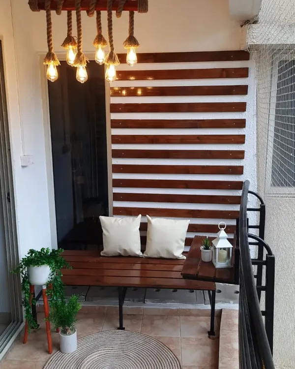 This urban balcony makeover features a custom-built pinewood bench and a matching slatted wall panel. The warm wood tones and industrial-style hanging lamp create a modern yet comfortable atmosphere.