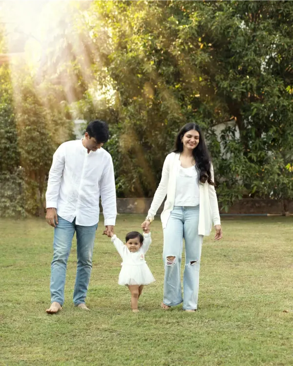 A heartwarming photo of parents holding their little girl's hands as she takes her first steps across a sunlit park lawn.