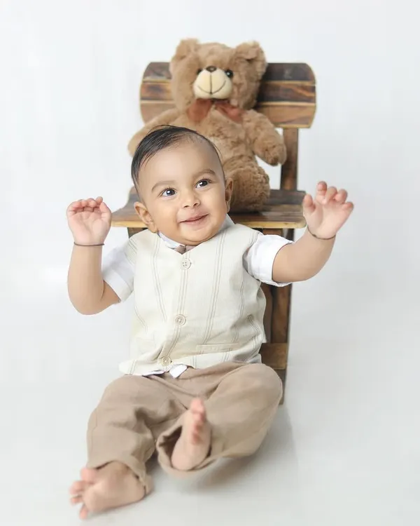A burst of pure happiness! This little boy's joyful expression and playful pose with his teddy bear is simply infectious.