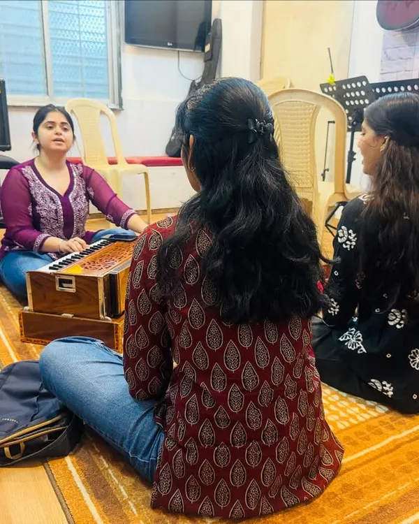 A Hindustani vocal class in session. Students sit with the instructor and a harmonium, learning the fundamentals of Indian classical singing in a traditional and focused setting.