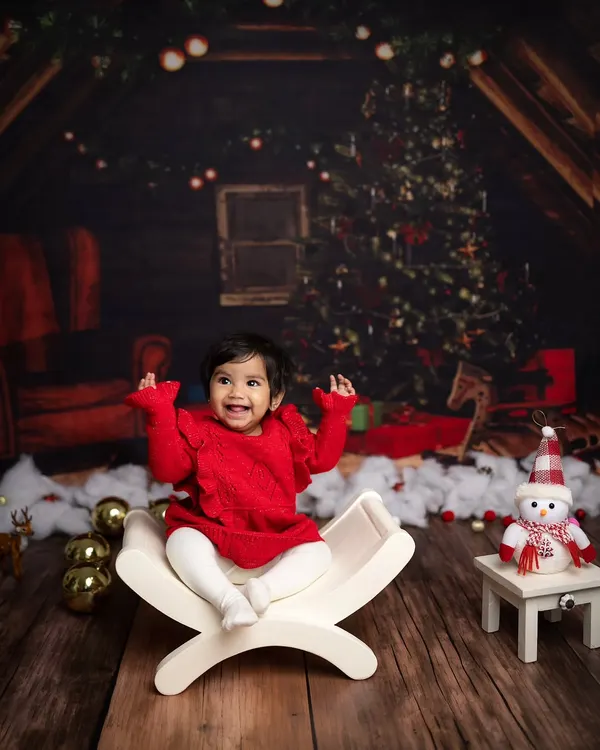A huge, joyful smile from this baby during her Christmas mini session. The cozy cabin backdrop and festive red outfit create a perfect holiday picture.